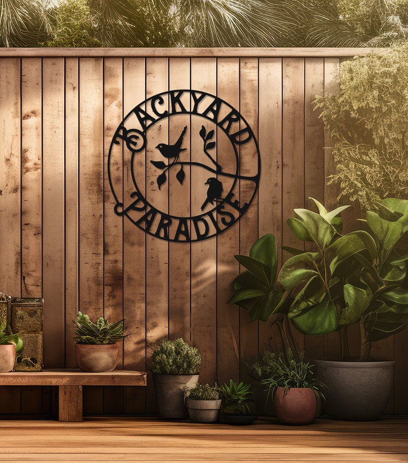 Black Backyard Paradise metal sign hanging on fence with plants